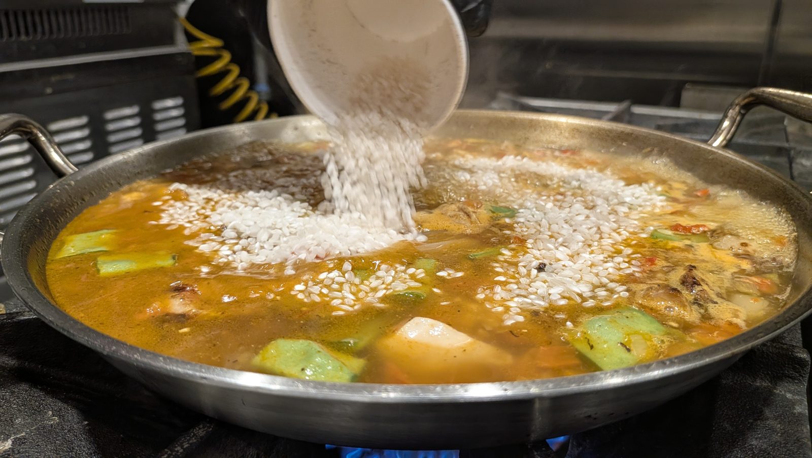 Rice poured from a container into the boiling stock.