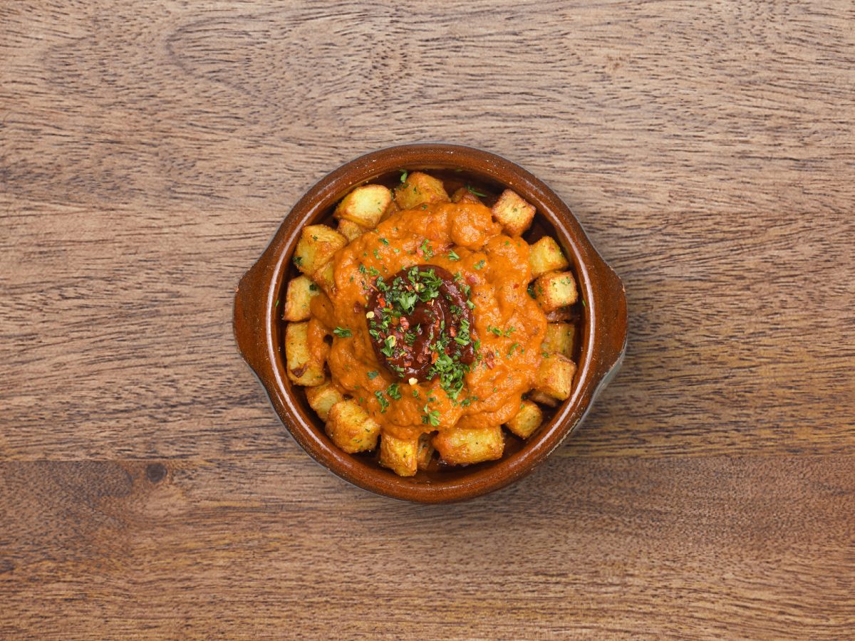 Patatas bravas in a terracotta dish: fried potatoes under spicy tomato sauce and aioli.
